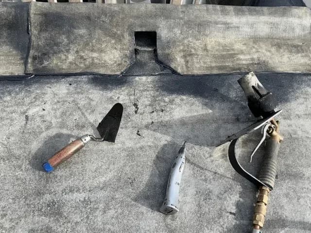 Troffel, kitmes en brander liggend op een bitumen dakbedekking langs een opstaande dakrand.